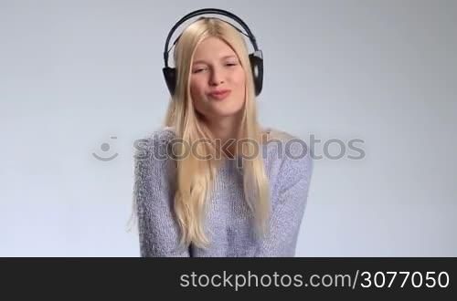 Emotional young woman in headphones listening to loud music and having fun on white background. Attractive girl moving to her music, dancing and smiling at camera, occasionally making funny face.