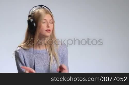 Emotional young woman with headphones listening to music over white background. Sweet girl with radiant smile looking at camera full of positive and joy while listening to music. Attractive female swaying along with music and gesturing to the rhythm.