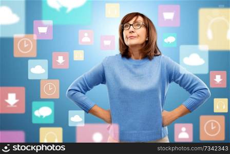 emotions and old people concept - displeased senior woman in glasses over app icons on blue background. displeased senior woman in glasses over app icons
