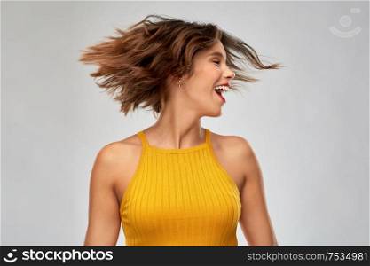 emotions and people concept - happy laughing young woman in mustard yellow top shaking head over grey background. happy young woman shaking head