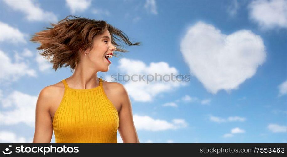 emotions and people concept - happy laughing young woman in mustard yellow top shaking head over blue sky and clouds background. happy young woman shaking head