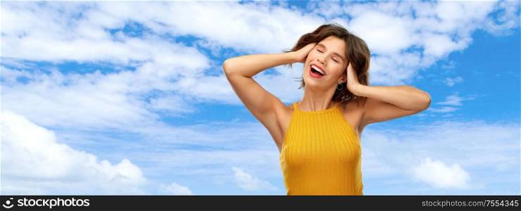 emotions and people concept - happy laughing young woman in yellow top over blue sky and clouds background. happy laughing young woman in yellow top over sky