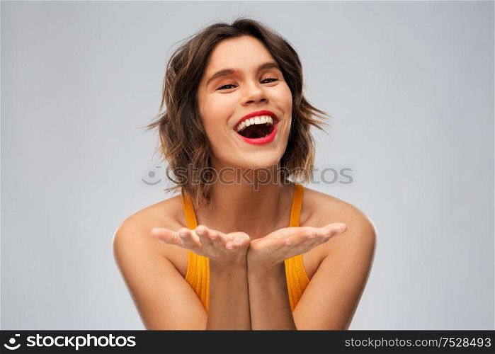 emotions and people concept - happy smiling young woman in mustard yellow top holding something on empty hands over grey background. happy young woman holding something on empty hands