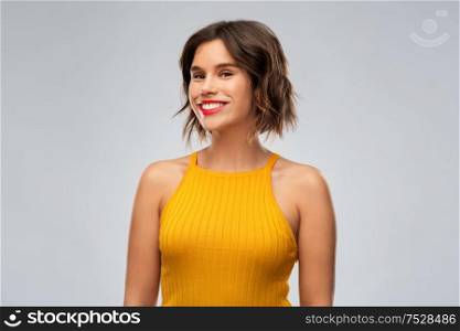 emotions and people concept - happy smiling young woman in mustard yellow top over grey background. happy smiling young woman in mustard yellow top
