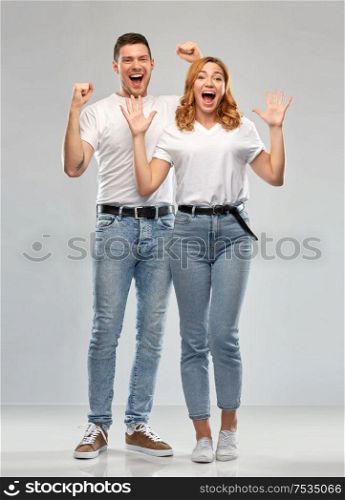 emotions and people concept - portrait of happy couple in white t-shirts celebrating success over grey background. portrait of happy couple in white t-shirts