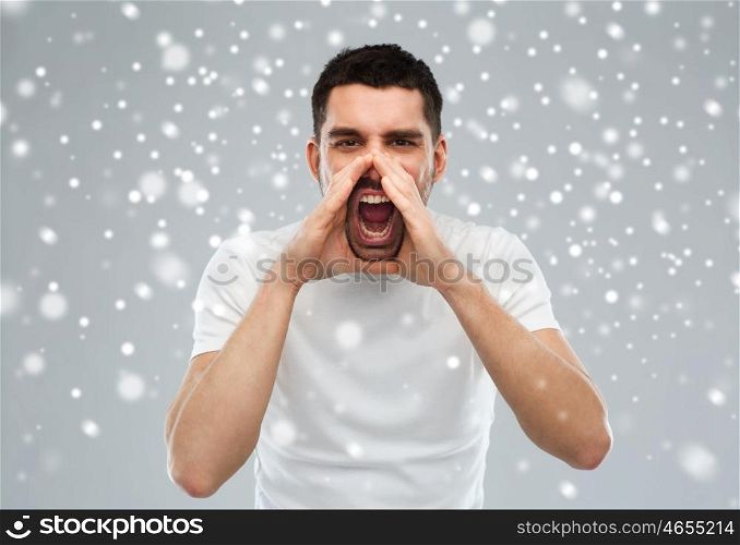 emotions, communication, winter, christmas and people concept - angry shouting man in t-shirt over snow on gray background