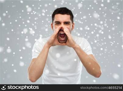 emotions, communication, winter, christmas and people concept - angry shouting man in t-shirt over snow on gray background
