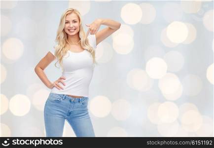 emotions, expressions, advertisement and people concept - happy smiling young woman or teenage girl in white t-shirt pointing finger to herself over holidays lights background