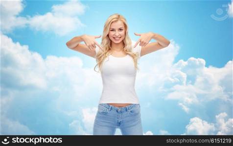 emotions, expressions, advertisement and people concept - happy smiling young woman or teenage girl in white t-shirt pointing finger to herself over blue sky and clouds background