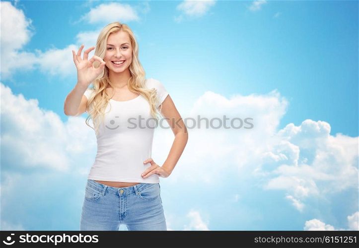 emotions, expressions, advertisement and people concept - happy smiling young woman or teenage girl in white t-shirt showing ok hand sign over blue sky and clouds background