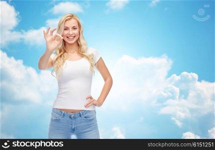 emotions, expressions, advertisement and people concept - happy smiling young woman or teenage girl in white t-shirt showing ok hand sign over blue sky and clouds background