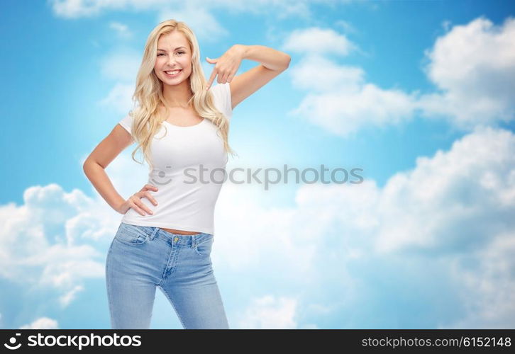 emotions, expressions, advertisement and people concept - happy smiling young woman or teenage girl in white t-shirt pointing finger to herself over blue sky and clouds background