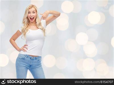 emotions, expressions, advertisement and people concept - happy smiling young woman or teenage girl in white t-shirt pointing finger to herself over holidays lights background