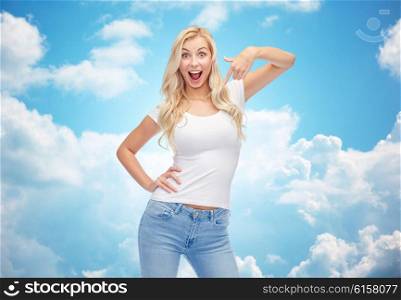emotions, expressions, advertisement and people concept - happy smiling young woman or teenage girl in white t-shirt pointing finger to herself over blue sky and clouds background