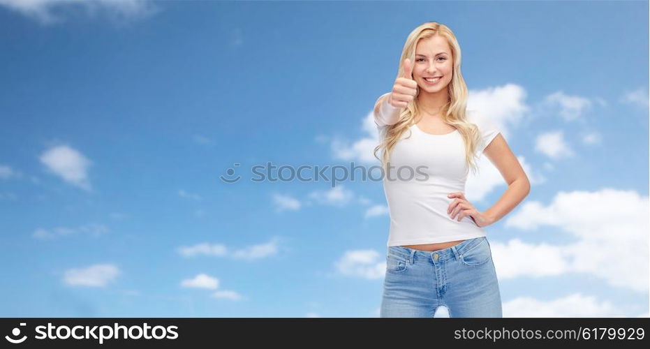 emotions, expressions, advertisement and people concept - happy smiling young woman or teenage girl in white t-shirt showing thumbs up over blue sky and clouds background