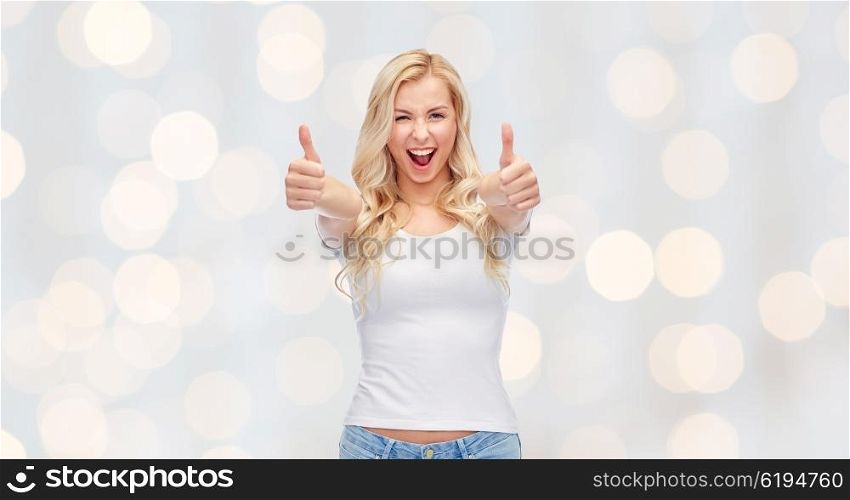 emotions, expressions, advertisement and people concept - happy smiling young woman or teenage girl in white t-shirt showing thumbs up with both hands over holidays lights background