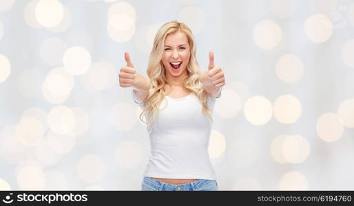 emotions, expressions, advertisement and people concept - happy smiling young woman or teenage girl in white t-shirt showing thumbs up with both hands over holidays lights background