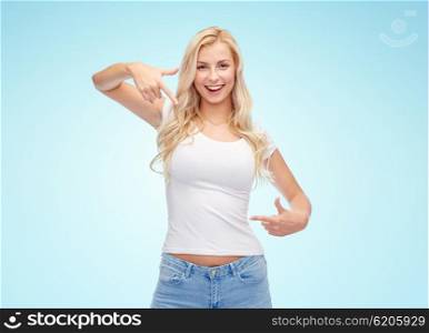 emotions, expressions, advertisement and people concept - happy smiling young woman or teenage girl in white t-shirt pointing finger to herself over blue background