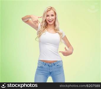 emotions, expressions, advertisement and people concept - happy smiling young woman or teenage girl in white t-shirt pointing finger to herself over green natural background
