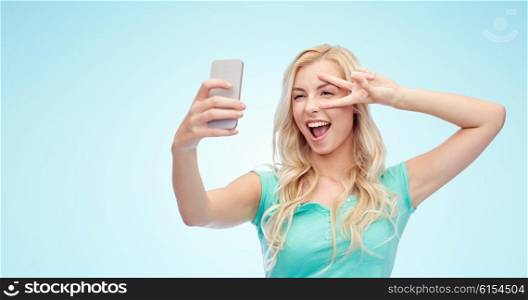 emotions, expressions and people concept - happy smiling young woman or teenage girl taking selfie with smartphone over blue background