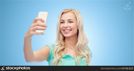 emotions, expressions and people concept - happy smiling young woman or teenage girl taking selfie with smartphone over blue background