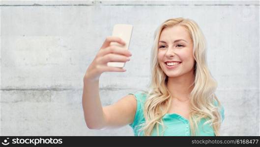 emotions, expressions and people concept - happy smiling young woman or teenage girl taking selfie with smartphone over gray concrete wall background