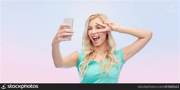 emotions, expressions and people concept - happy smiling young woman or teenage girl taking selfie with smartphone over rose quartz and serenity gradient background