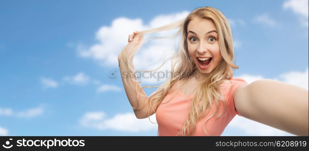 emotions, expressions and people concept - happy smiling young woman or teenage girl taking selfie over blue sky and clouds background
