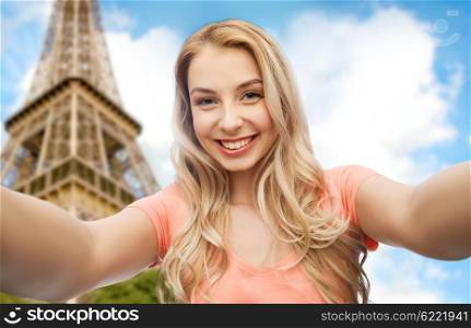 emotions, expressions and people concept - happy smiling young woman taking selfie over paris eiffel tower background