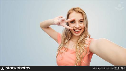 emotions, expressions and people concept - happy smiling young woman taking selfie and showing peace hand sign over gray background