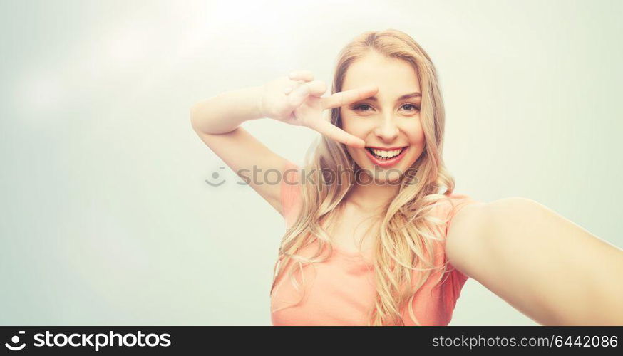 emotions, expressions and people concept - happy smiling young woman taking selfie and showing peace hand sign over gray background. smiling woman taking selfie and showing peace sign