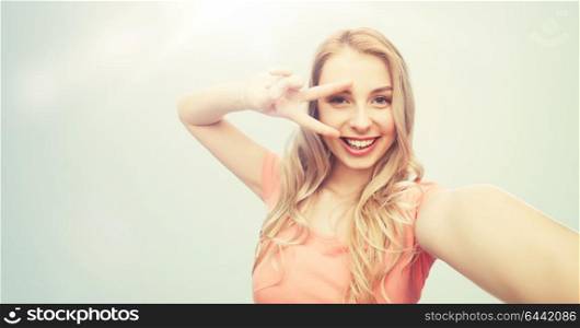 emotions, expressions and people concept - happy smiling young woman taking selfie and showing peace hand sign over gray background. smiling woman taking selfie and showing peace sign