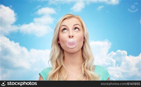 emotions, expressions and people concept - happy young woman or teenage girl chewing gum over blue sky and clouds background