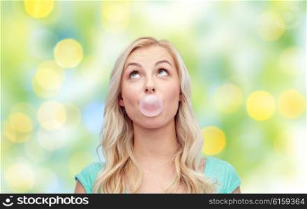 emotions, expressions and people concept - happy young woman or teenage girl chewing gum over summer green lights background