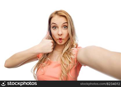 emotions, expressions and people concept - happy young woman taking selfie, making fish face and showing thumbs up