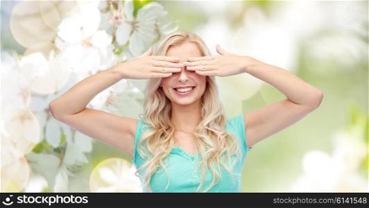 emotions, expressions and people concept - smiling young woman or teenage girl covering her eyes with palms over natural spring cherry blossom background
