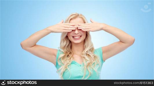 emotions, expressions and people concept - smiling young woman or teenage girl covering her eyes with palms over blue background
