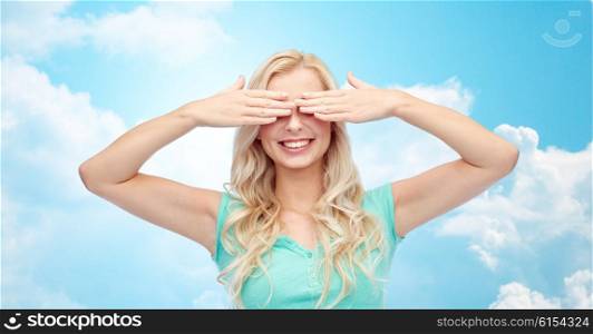 emotions, expressions and people concept - smiling young woman or teenage girl covering her eyes with palms over blue sky and clouds background