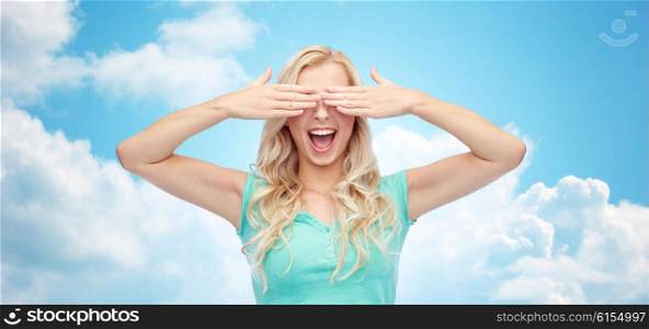 emotions, expressions and people concept - smiling young woman or teenage girl covering her eyes with palms over blue sky and clouds background