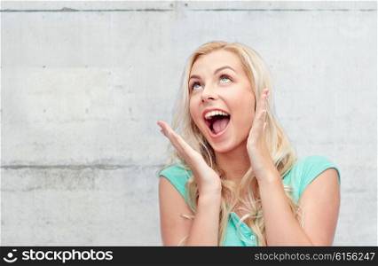 emotions, expressions and people concept - surprised smiling young woman or teenage girl over gray concrete wall background