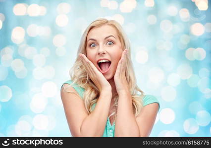 emotions, expressions and people concept - surprised smiling young woman or teenage girl over blue holidays lights background