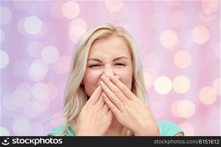 emotions, expressions, embarrassment, and people concept - young woman or teenage girl wrinkling and closing her nose of unpleasant smell over pink holidays lights background