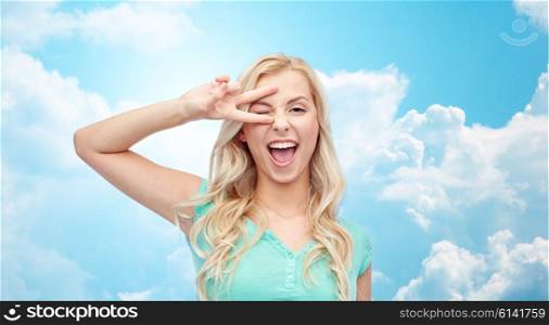 emotions, expressions, gesture and people concept - smiling young woman or teenage girl showing peace hand sign over blue sky and clouds background
