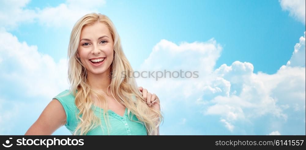 emotions, expressions, hairstyle and people concept - smiling young woman or teenage girl holding her strand of hair over blue sky and clouds background
