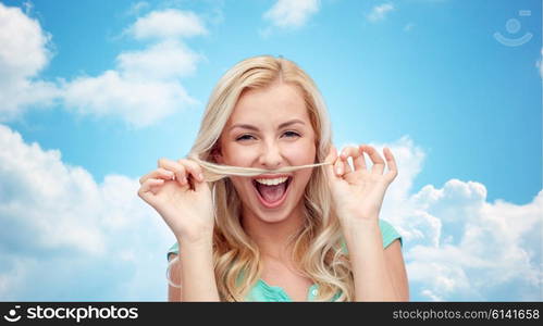 emotions, expressions, hairstyle and people concept - smiling young woman or teenage girl making mustache with strand of hair over blue sky and clouds background