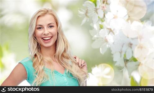 emotions, expressions, hairstyle and people concept - smiling young woman or teenage girl holding her strand of hair over natural spring background