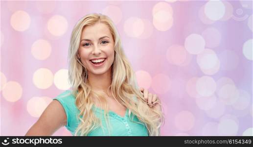 emotions, expressions, hairstyle and people concept - smiling young woman or teenage girl holding her strand of hair over pink holidays lights background