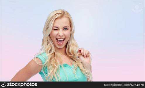 emotions, expressions, hairstyle and people concept - smiling young woman or teenage girl holding her strand of hair and winking over rose quartz and serenity gradient background