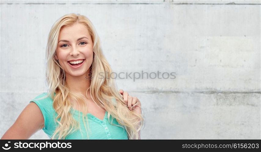 emotions, expressions, hairstyle and people concept - smiling young woman or teenage girl holding her strand of hair over gray concrete wall background
