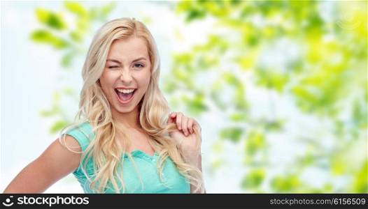 emotions, expressions, hairstyle and people concept - smiling young woman or teenage girl holding her strand of hair and winking over green natural background